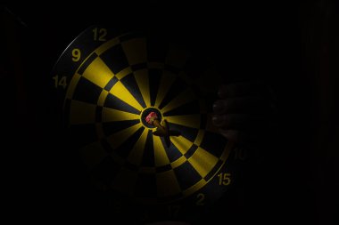 Karanlıkta dart ve dart ve merkezde bir ışık demeti ve bir kadının eli.