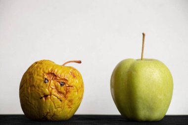 A rotten and sluggish apple with a sad painted smile and a fresh ripe green apple next to it on a white background on a black table, bad and good apples, a choice clipart