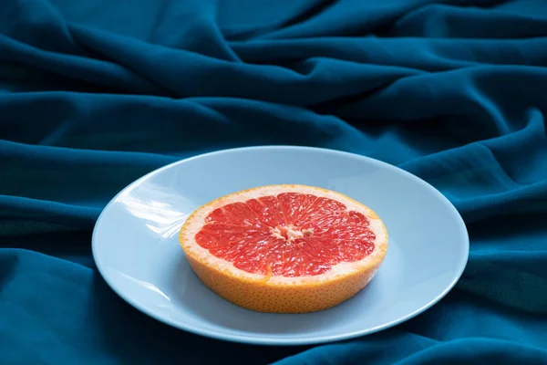 グレープフルーツのスライスは フルーツ ビーガンフードとして重い青いテーブルクロスのプレートの上にあります — ストック写真