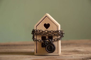 Ev zincire vurulmuş, asma kilit altında ve ahşap bir tahtanın üzerinde duruyor. Gayrimenkul satışı yasağı konsepti, ev koruması.