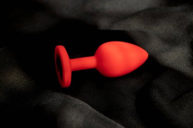 Kırmızı silikon pürüzsüz anal dolgu, seks oyuncağı, gölgede siyah bir arka plan. Anal oyuncaklar, erotik oyuncaklar.