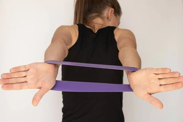 The girl is engaged in fitness with a fitness rubber band on a white background, hands and posture with a fitness rubber band, trains