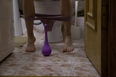 Kız tuvalette oturuyor ve yanında da lavman, bağırsak temizleme var.