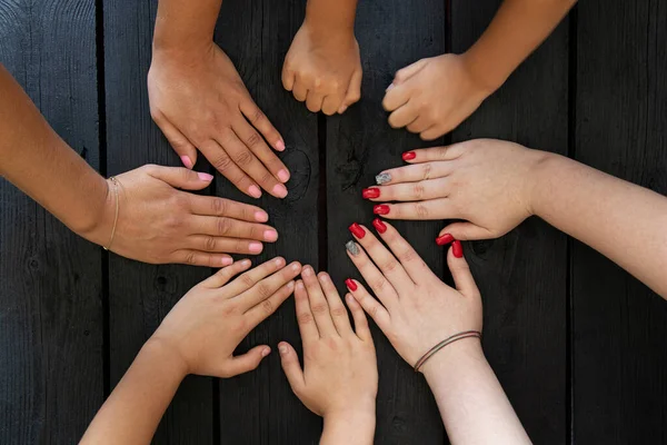 Female hands and child\'s hands on a wooden black board as a team, strength and unity of the family, teams, many hands