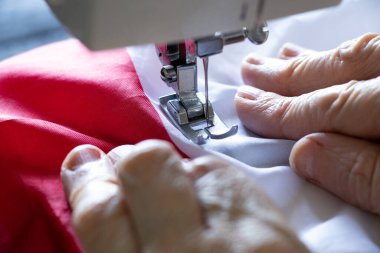 Yaşlı bir kadının elleri dikiş makinesine Polonya bayrağını dikiyor.