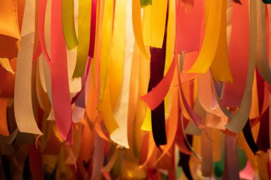 Çok renkli kurdeleler lambaların ışığında bir zemin olarak asılı, kurdelelerden neşeli bir dekor.