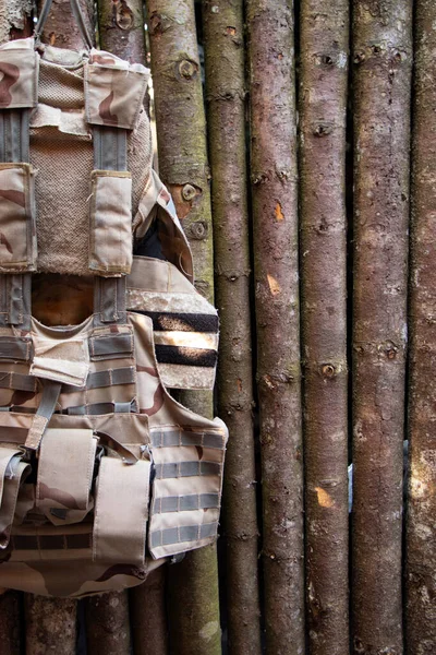 An old worn-out soldier's vest hangs on a wooden wall made of logs, a worn-out army military vest