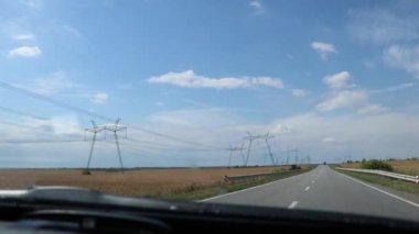 Yazın Ukrayna 'daki güç iletim kulesi. Yüksek gerilimli güç iletim hattı teçhizatı bir tarla boyunca destekliyor, yol boyunca giden bir arabanın içinden görüş sağlıyor.