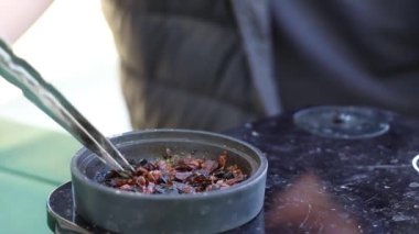 Bir adam yazın güneşte sokakta nargile yapar, nargile tütünü karıştırır, nargile içer.