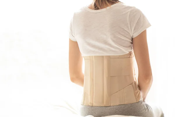Woman with a corset on her back to support her back from pain in the back and spine, Medical concept, spinal support, back pain, wearing a brace at home