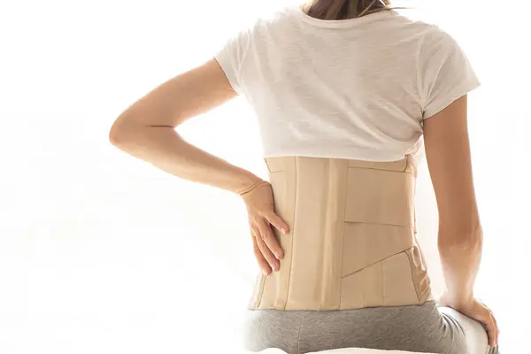 Woman with a corset on her back to support her back from pain in the back and spine, Medical concept, spinal support, back pain, wearing a brace at home
