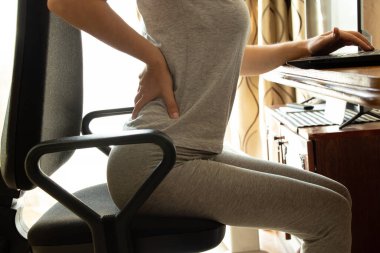 Sırtı ve omurgası ağrıyan bir kadın çalışırken bilgisayar sandalyesinde oturuyor. Tıbbi konsept, omurga desteği, sırt ağrısı.