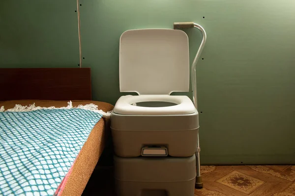 A portable plastic dry closet stands near the bed in the bedroom for an elderly person who has difficulty walking, dry closet, comfort