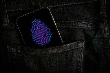 Gri kot pantolonlar, veri güvenliği, teknoloji ve şifrenin cebinde parmak izi olan bir telefon var.