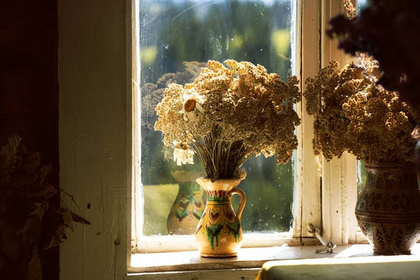 Dry flowers in an old vase stand in an old house on the window during the day in the sunlight in the Carpathians in Ukraine