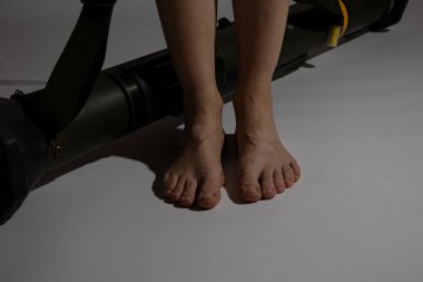 Ukrayna 'daki savaşta kullanılan bir el bombası fırlatıcı gölgelerde beyaz bir arka planda ve yakınlarda çıplak ayaklı bir kadın, tanksavar silahı, savaş bombası atar.