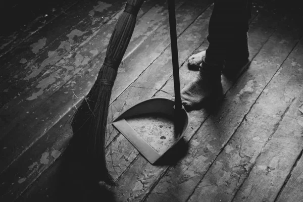 Womens feet on the floor and a broom and dustpan nearby, a girl sweeping the floor of the house, black and white photo, cleaning