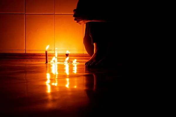 A girl sits on the floor in the dark with candles in an apartment in the dark without light in Ukraine, sitting on the floor alone in the dark, feet on the floor