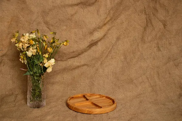 Empty portioned wooden plate, vase with dried flowers on burlap background, minimalistic background for display