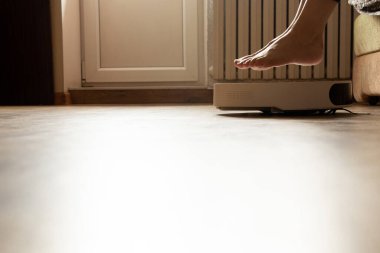 Dişi bacaklar ve yerde robot bir elektrikli süpürge. Daireyi temizliyor, evi temizliyor.