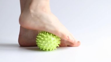 Bir kız ayaklarına beyaz arka planda sivri uçlu lastik bir topla masaj yapıyor, ayak masajı, spor ve sağlık.