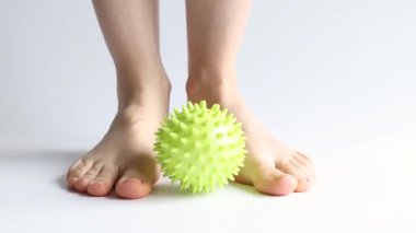 Bir kız ayaklarına beyaz arka planda sivri uçlu lastik bir topla masaj yapıyor, ayak masajı, spor ve sağlık.