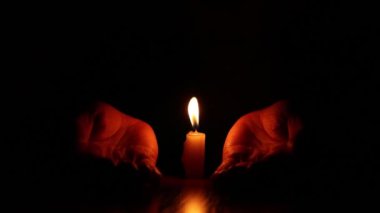 Karanlığın içinde bir mum alevinin yanında kadınların elleri, inanç ve din, dua.