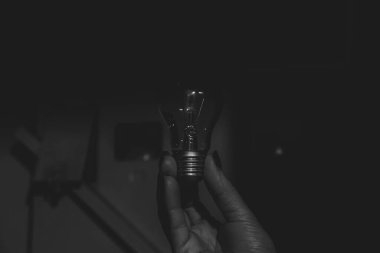 An incandescent lamp in the hands of a girl in the corridor near the meter, black and white photo, without light in Ukraine