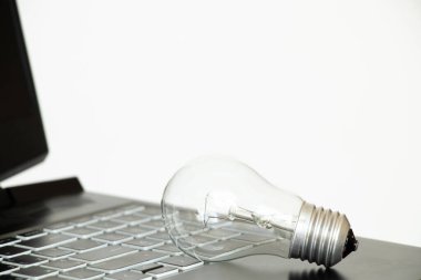 Beyaz zemin üzerinde parlak ampul ve siyah laptop, ışığın fiyatı, elektrik