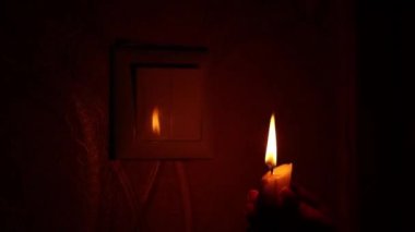 Elinde mum olan bir kadının eli karanlıkta ışık düğmesini açar ve kapatır. Işıksız Ukrayna, elektrik kesintisi.