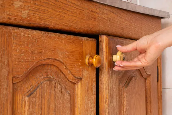 stock image Female hand opens brown old kitchen cabinet in kitchen in apartment, kitchen furniture