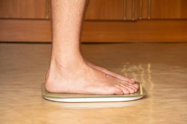Bir adam bir apartmanın zemininde bir terazide duruyor, kilosunu izliyor, diyet yapıyor.