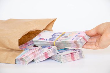Bir kadının eli, beyaz bir arka planda, para ve kârda, 200 hryvnia 'lık desteler halinde bir kese kağıdının içinde yatan Ukrayna hryvnialarını çıkarır.