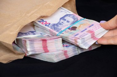 Bir kadının eli, siyah bir arka planda, para ve karla kaplı bir kese kağıdında yatan Ukrayna hryvnialarını paketler halinde 200 hryvnias çıkarır.