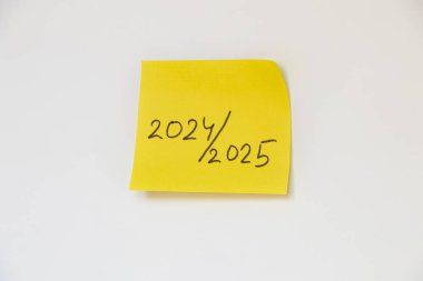 2024 ve 2025 sarı kağıda yazılmış, beyaz arka plana yapıştırılmış, yeni ve eski yıla