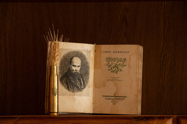 Украина Днепр 09 февраля 2025 года - Книга Кобзаря Тараса Шевченко и гильза с гербом Украины и ухом пшеницы на полке