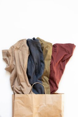 Kırışmış dört pamuklu tişört mavi, bej, zeytin ve kırmızı renkte beyaz arka planda, kıyafetlerde, günlük tişörtlerde bir kese kağıdında yatıyor.