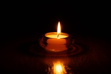 Camda yanan mum yuvarlak şamdan. Evdeki masada, karanlıkta, mum alevi.