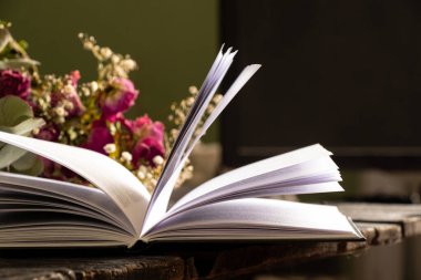 Evdeki ahşap masada açık bir kitap ve odada kuru güller var.