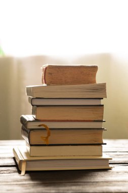 Evdeki ahşap bir masanın üzerinde bir yığın kitap, kitaplar.