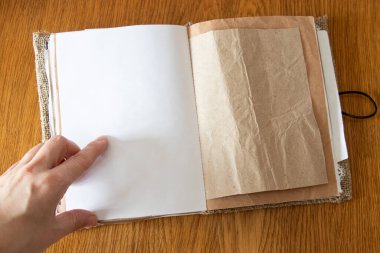 Kadın eli, Kraft kağıdı ve ahşap masa üzerindeki çuval bezinden yapılmış boş defterdeki sayfayı işaret ediyor.