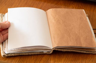 Kadın eli, Kraft kağıdı ve ahşap masa üzerindeki çuval bezinden yapılmış boş defterdeki sayfayı işaret ediyor.