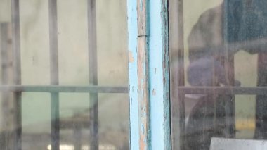İş üniformalı bir ressam bir boyacıda boya karıştırıyor ve tartıyor, sokaktan kirli bir pencereye bakıyor, boyacı dükkanını boyuyor.