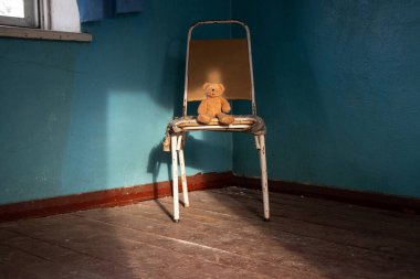 Ukrayna 'da terk edilmiş eski bir evde sandalyede oturan kahverengi oyuncak ayı unutulmuş, terk edilmiş bir oyuncak.