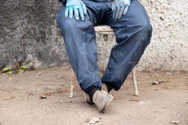 İşçi üniformalı kirli erkek ressam sokakta bir sandalyede oturur dinlenir, kırılır, erkek bacakları kırılır, sıkı çalışır.