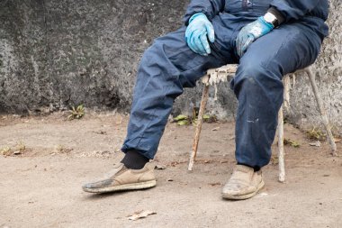 İşçi üniformalı kirli erkek ressam sokakta bir sandalyede oturur dinlenir, kırılır, erkek bacakları kırılır, sıkı çalışır.