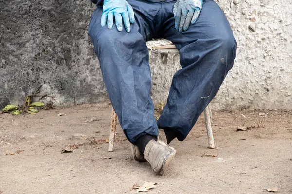 İşçi üniformalı kirli erkek ressam sokakta bir sandalyede oturur dinlenir, kırılır, erkek bacakları kırılır, sıkı çalışır.