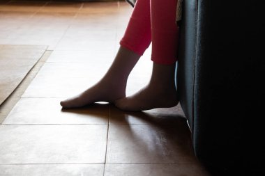 Küçük kızın ayakları yerde. Yatak odasındaki kanepede oturuyor. Işıkta.