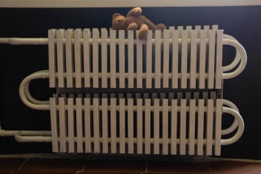 Yatak odasının penceresinin altındaki dairede eski beyaz radyatör ve bataryasında bir oyuncak ayı, merkezi ısıtma, sıcak bir ev.