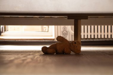 Terk edilmiş bebek kahverengi oyuncak ayı yatak odasında yatağın altında, oyuncak ayı yatağın altında.
